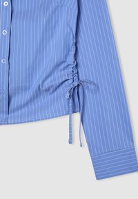 Camicia a maniche lunghe blu a righe con un frontale a bottoni e dettaglio arricciato con cordoncino laterale vicino all'orlo.