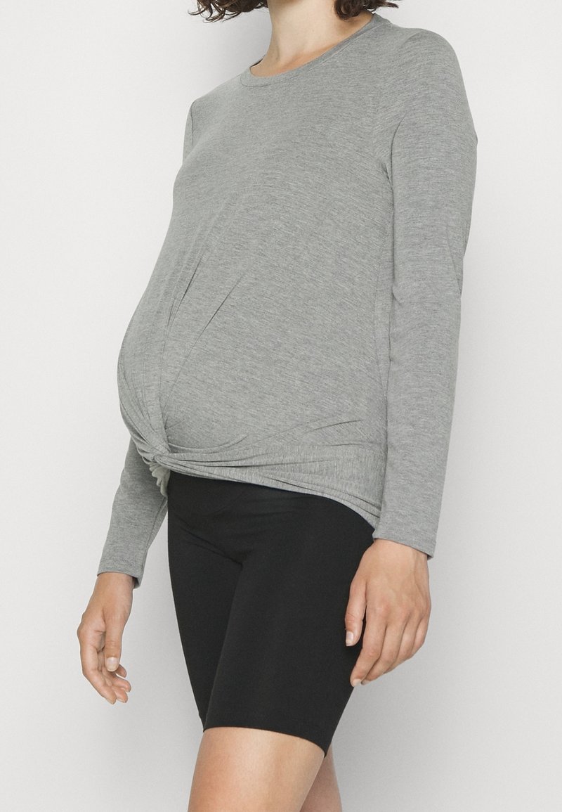 Chemise à manches longues grise avec un devant torsadé, associée à un short de cyclisme noir. Tissu doux, coupe décontractée, conçue pour le port de maternité.
