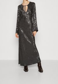 Lång svart klänning med en djup nyckelhålsringning, långa ärmar och ett slätt, texturerat tyg med ett abstrakt mönster.