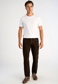 Biała bawełniana koszulka zestawiona z ciemnobrązowymi spodniami z korduroju i brązowymi skórzanymi butami na sznurówki. Model stoi z ramionami swobodnie opuszczonymi wzdłuż ciała.