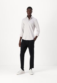 Ljusgrå, långärmad skjorta med knappar och krage, tillsammans med svarta, tapered byxor och vita sneakers. Slät tyg med subtil struktur.