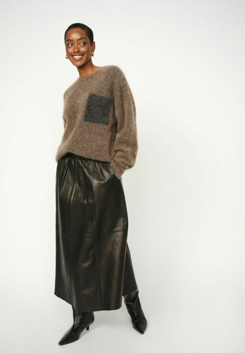 Bruin mohair sweater met een donkergrijze zak, gecombineerd met een zwarte leren rok en zwarte puntige laarzen. Glad, textuur materiaal.