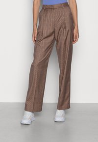 Bruna rutiga byxor med veck, hög midja, vida ben och en mjuk textur. Matchas med vita sneakers.