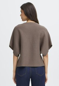 Brun, ribbad stickad topp med bred båtsträng och oversized ärmar, kombinerad med mörkblå denim, som visar en slät textur och avslappnad passform.