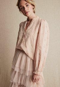 Rosa blus med blommig broderi, volangkrage, långärmad, tillsammans med en lager av tyllekjol i en liknande nyans. Subtil textur och design.