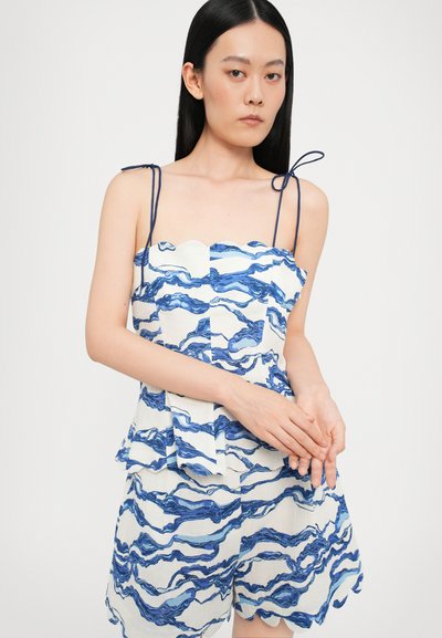 Blå og hvit mønstret topp med bølgete kanter og bånd. Har bølgede design og en peplum-stil silhuett som er kombinert med matchende shorts.
