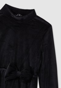 Abito nero a coste con collo alto, maniche lunghe e un evidente fiocco in tessuto in vita. Tessuto morbido.