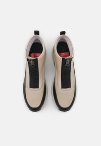 Bottines beiges et noires avec fermeture éclair, en cuir, de forme arrondie, avec des détails texturés et des accents contrastés.