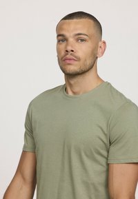 T-shirt vert olive à col rond, à manches courtes et texture de tissu lisse. Design simple sans motifs ou accents visibles.