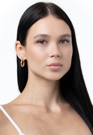 Orecchini a cerchio in oro con un design testurizzato e accenti scintillanti. Il modello ha capelli neri lunghi e lisci e tonalità di pelle neutre.