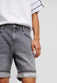Pantalones cortos de mezclilla en gris deslavado con un dobladillo enrollado, que cuentan con un bolsillo frontal, presillas para cinturón y el texto blanco "KARL LAGERFELD JEANS" en el costado.