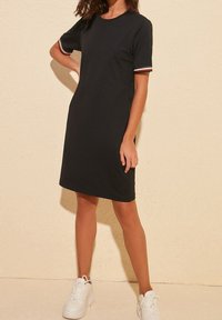 Černé bavlněné šaty s krátkými rukávy, ozdobené červenobílými pruhovanými detaily na manžetách. Jednoduchý střih rovného střihu, délka do kolen.