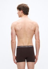 Καφέ ανδρικά μπόξερ από μαλακό υλικό, με μαύρη μέση που φέρει το λογότυπο «KARL LAGERFELD», εμφανιζόμενα από πίσω σε ανδρικό μοντέλο.