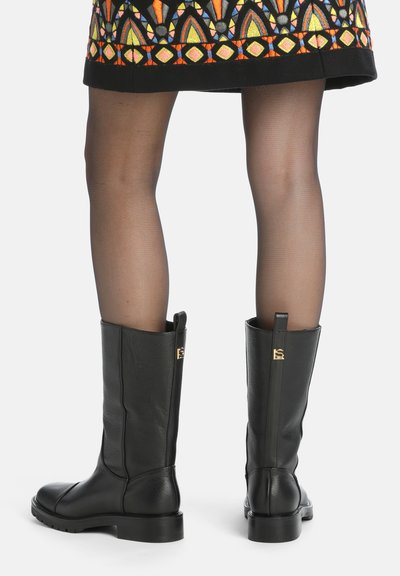 Botas de cuero negras hasta la rodilla con una textura suave, punta redondeada y una suela resistente. Presentan un acento decorativo dorado en la parte trasera.