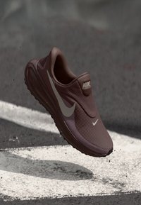 Παπούτσι Nike σε σκούρο μπουρντό χρώμα, με υφή στην επιφάνεια, σχεδιασμό τύπου slip-on, λευκό λογότυπο swoosh και ελαφριά κατασκευή.