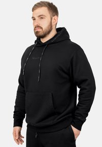 Felpa nera in cotone con tasca frontale, cappuccio con cordino e logo ricamato sul petto. Presenta polsini e orlo a coste.