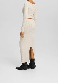 Knitted cream two-piece outfit featuring a fitted long-sleeve top and a long skirt with a side slit, paired with black ankle boots.