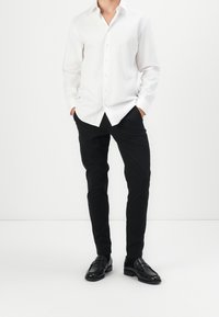 Weißes Kurzarmhemd mit glatter Textur, schwarze Slim-Fit-Hosen und schwarze Slipper, die ein klassisches Design und klare Linien aufweisen.