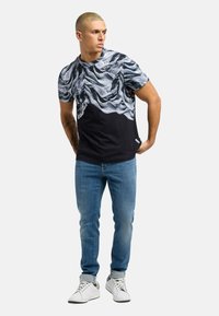 T-skjorte med korte ermer som har et strukturert svart og hvitt abstrakt mønster på toppen, solid svart bunn, sammen med blå jeans og hvite joggesko.