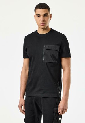 Sort T-shirt med rund hals, der har en tekstureret sort lynlåslomme på venstre bryst og korte ærmer.