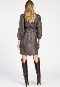 Korte bruine jurk met een taille accent, opbollende lange mouwen en donkerbruine kniehoge laarzen met hoge hakken, met puntige toppen en een gestructureerd patroon.