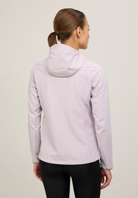 Hellblaues Softshell-Jackett mit einer taillierten Silhouette, verstellbarem Kapuze und reflektierenden Akzenten, kombiniert mit schwarzen Leggings.