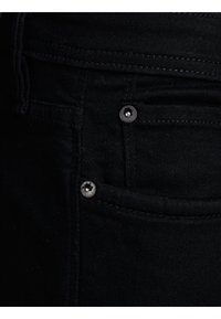 Gros plan sur la poche en denim noir montrant les coutures et deux rivets en métal.