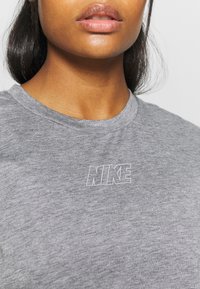 Šedé bavlněné tričko s jemným bílým logem Nike na levé straně. Tkanina má hladkou strukturu a klasický kulatý výstřih.