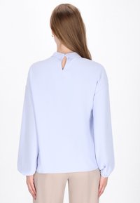 Lys blå bluse med lange, puffede ærmer og en nøglehul bagside. Glat, blødt stof med en afslappet, oversized pasform.