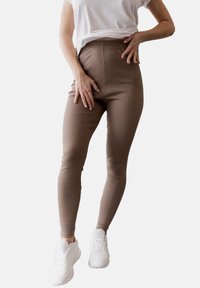 Brązowe legginsy z wysokim stanem o prążkowanej fakturze, w połączeniu z białymi sneakersami, charakteryzujące się dopasowanym krojem zapewniającym komfort i swobodę ruchów.