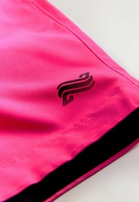 Rosa athletische Shorts mit glatter Textur, versehen mit einem schwarzen Logo und kontrastierendem schwarzen Saum. Nahaufnahme betont Farbe und Designdetails.