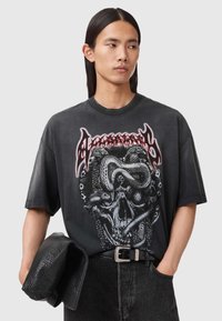 Zwart oversized T-shirt met een grafisch ontwerp van een schedel verweven met slangen, met een ronde halslijn en korte mouwen. Draagt donkere spijkerbroek.