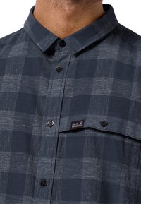 Rutig knappskjorta i marinblått med vita ränder. Tillverkad av bomull, med en bröstficka och en logotag på framsidan.