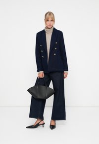 Marineblå dobbeltspent blazer, beige turtleneck, vide mørke denim bukser, sorte slingback-sko og en sort strukturert håndveske.