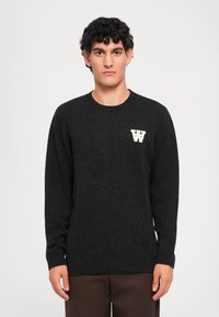 Mørkegrå genser med rund hals og ribbede mansjetter, med en liten hvit "W"-logo på venstre bryst. Glatt strikket tekstur.