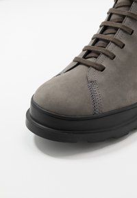 Bottine en suède gris avec semelle en caoutchouc noir. Caractéristiques : bout arrondi, design à lacets et détail de couture contrastante sur le côté.