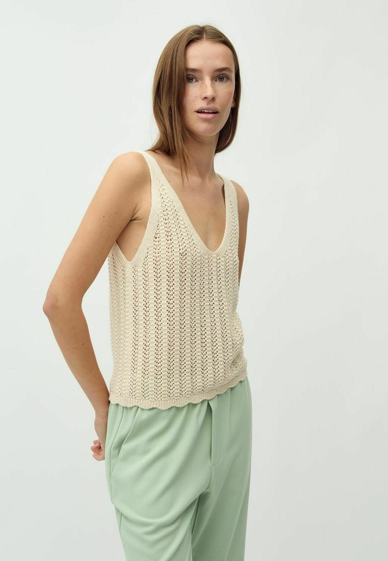 Cremfarbener gestrickter Tank-Top mit V-Ausschnitt und offenen Seiten, ausgestattet mit einem strukturierten Muster, kombiniert mit lockeren mintgrünen Hosen.