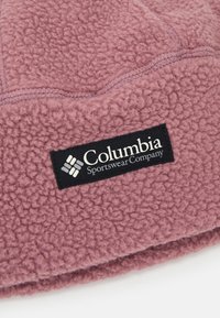 Fleece beanie i myk mauve, med en teksturert overflate og et svart Columbia Sportswear-merke. Uthevet med broderte detaljer.