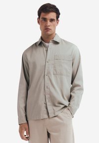 Lichtgrijs langarmig shirt van zachte stof, met een knoopsluiting aan de voorkant, een enkele borstzak en een relaxte pasvorm.
