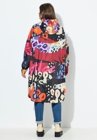 Manteau de pluie surdimensionné multicolore avec capuche, présentant des motifs abstraits en rouge, bleu, orange et noir, fabriqué en tissu léger.