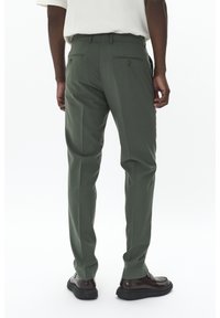 Pantalons ajustés à plat en tissu vert foncé. Dotés de deux poches arrière et d'une texture lisse. Assortis à des chaussures noires.