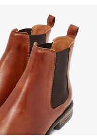 Botas Chelsea de cuero marrón con paneles laterales elásticos, lengüetas y un tacón apilado. Textura suave con acentos contrastantes en negro.