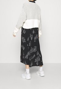 Jupe noire ornée de figures blanches en dessin linéaire, associée à un pull court gris et crème. Manches larges et coupe décontractée. Des baskets blanches complètent le look.