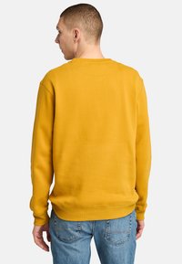 Gul sweatshirt med rund halsringning, ribbade ärmslut och nederkant; visad bakifrån, kompenserad med ljusblå jeans. Slät tygstruktur.