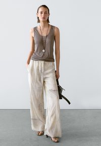 Lichtgrijze tanktop, losse crème wijde broek met subtiele textuur, gelaagde hangerssieraden en sandalen met bandjes. Minimalistisch ontwerp.