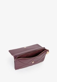 Portafoglio in pelle bordeaux con motivo trapuntato, chiusura con zip e dettagli in tonalità oro. Presenta un ampio interno con fodera.