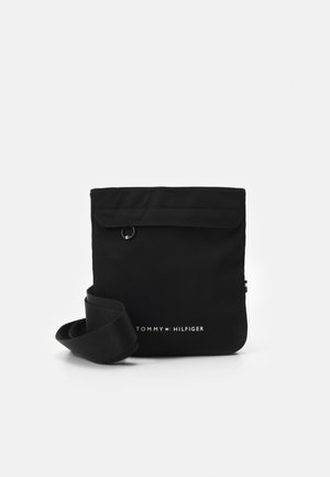 Borsa a tracolla nera in nylon con chiusura a pattina, caratterizzata da un accento in anello d'argento e logo "TOMMY HILFIGER" in bianco sulla parte frontale.