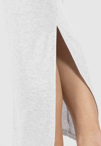 Nærbillede af et ben synligt gennem et lårhøjt slid i et lysegråt ribbet stof, nederdel eller kjole.