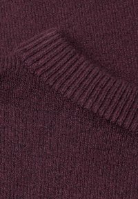 Gros plan sur un tissu tricoté côtelé bordeaux doux avec une partie pliée montrant la texture et les détails des coutures.