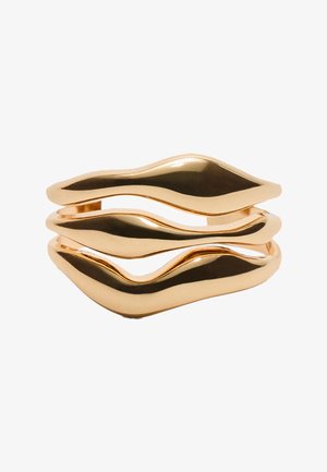 Anello ondulato in oro realizzato in metallo lucido, con tre fasce curve caratterizzate da una superficie liscia e brillante e da un design ondulato.